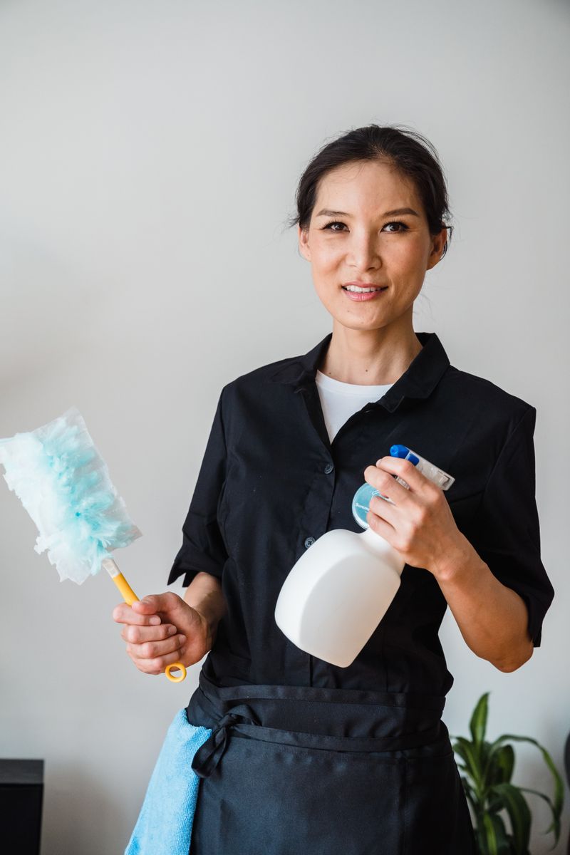 A cleaning professional in uniform holding a duster and spray bottle, ready to start a job.