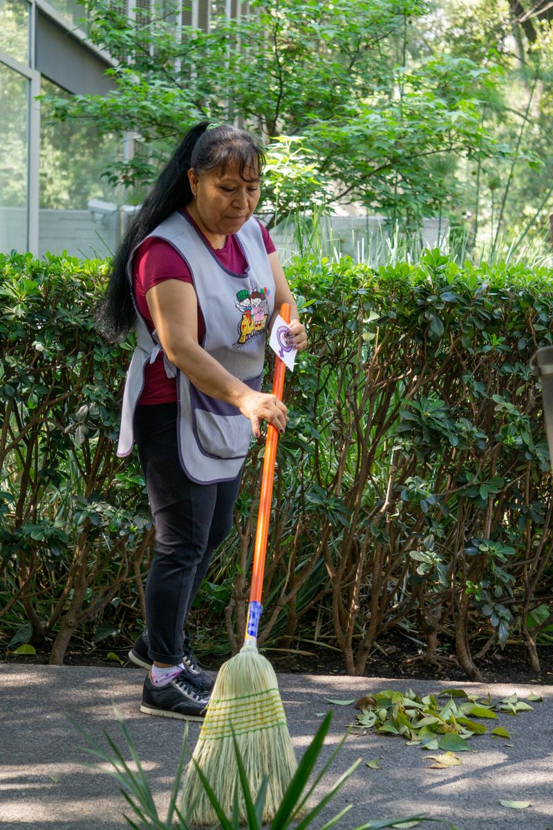 A cleaning professional sweeping outside a commercial building in a green, well-kept setting.
